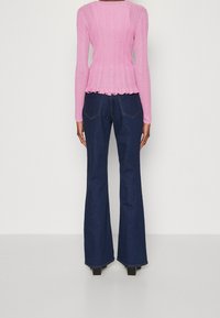 Strak roze geribd shirt met lange mouwen en golvende zoom, gecombineerd met donkerblauwe uitlopende jeans met achterzakken en zichtbare naaddetails.