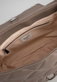 Quiltet beige håndtaske lavet af syntetisk materiale, med en rummelig indvendig plads, en lynlås lomme og et mærke. Sølv hardware detaljer.