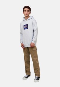 Grå hoodie med en logotyp på framsidan, beige cargo byxor och svarta sneakers. Avslappnad stil med luftig passform och mjuk textur.