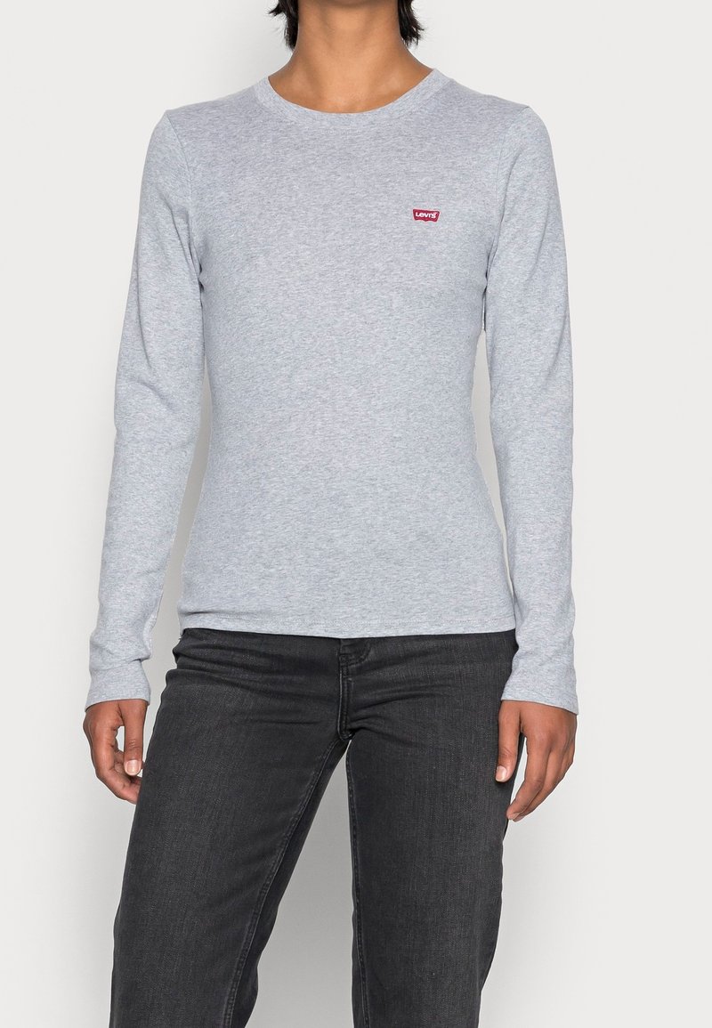 Vaaleanharmaa pitkähihainen puuvillapaita, jossa on pyöreä kaula-aukko ja pieni punainen Levi's-logo vasemmassa rinnassa. Yhdistetty mustiin farkkuihin.