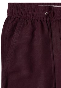 Gros plan sur un pantalon bordeaux avec ceinture élastique, cordon de serrage et poche latérale visible.