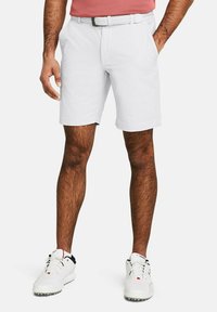 Weiße Shorts aus einem glatten Stoff, mit Seitentaschen, flachem Bund und einem passenden Gürtel. Kombiniert mit weißen Golfschuhen.