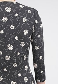 Zwarte jurk met witte bloemenprint, voorzien van lange mouwen, een ronde halslijn en een gladde stofstructuur.