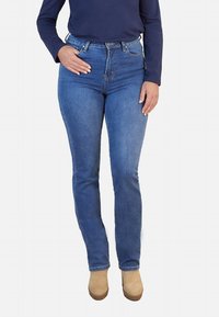 Jeans skinny de mezclilla azul con cintura alta, diseño de cinco bolsillos y un ligero desgastado. Combinados con zapatos de plataforma color beige.