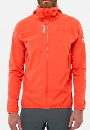 Homme portant une veste zippée orange vif avec un col haut et des logos blancs "MILLET" sur la poitrine et la manche gauche, debout devant un fond blanc.
