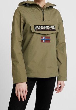 Person trägt olivgrüne Kapuzenjacke mit Klappe an der Fronttasche mit der Aufschrift „Napapijri geographic“ und einem Norwegen-Flaggen-Patch darunter.