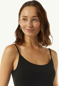 Camisola nera con spalline sottili, realizzata in un tessuto morbido e liscio. Girocollo e design semplice, perfetta per essere indossata a strati.