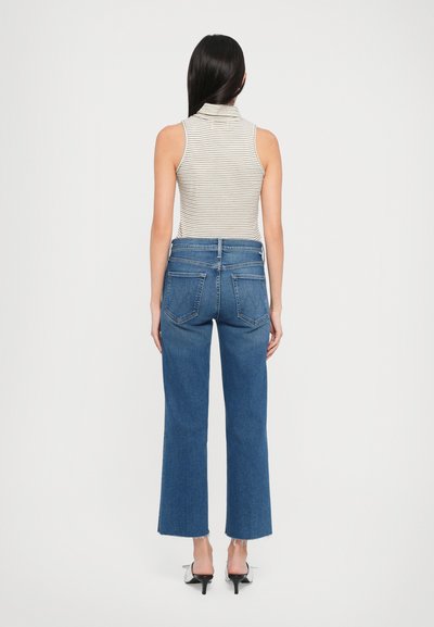 Top a strisce senza maniche con colletto; abbinato a jeans blu a vita alta con taglio dritto e orlo sfilacciato, indossati con tacchi neri.