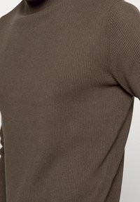 Pull en tricot côtelé marron avec un col haut. Présente un design ajusté et une épaisseur moyenne. La texture est lisse avec un léger extensibilité.