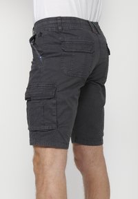 Man som bär mörkgrå cargo-shorts med flera fickor och en vit skjorta, visad från midjan ner och bakifrån.