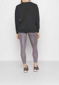 Czarny sweter z raglanowymi rękawami, w połączeniu z błyszczącymi jasnofioletowymi legginsami i ciemnymi butami sportowymi, sfotografowany z tyłu.