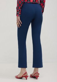 Eine Frau trägt taillierte marineblaue Hosen, rote Slingback-Schuhe mit Kitten-Heel und eine gemusterte Langarmbluse mit roten und marineblauen Kreisen.