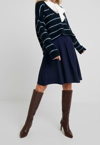 Marinrandig fluffig tröja med vida ärmar, parat med en knälång kjol och bruna spetsiga högklackade stövlar.