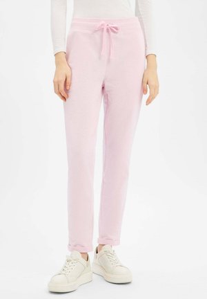 Hellrosa Jogginghose mit elastischem Bund und verstellbarem Kordelzug. Weicher Stoff, verjüngtes Bein und Bündchen, die über weißen Sneakern hochgekrempelt sind.