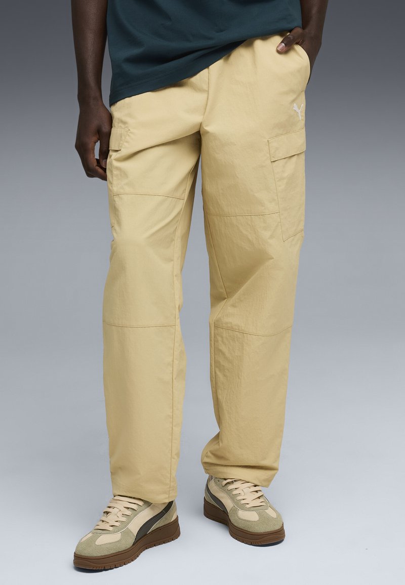 Beige cargo bukser i letvægtsstof med flere lommer, der har en afslappet pasform og synlige sømdetaljer, parret med retro-stil sneakers.
