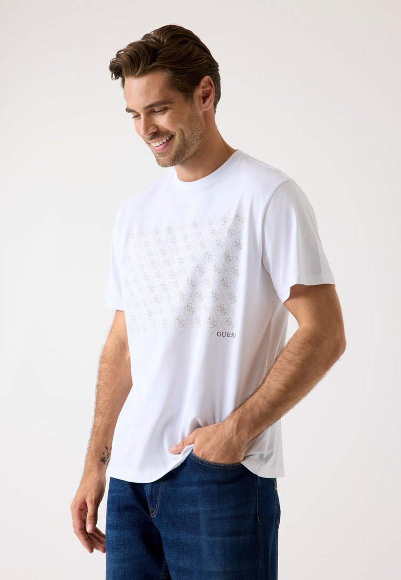 Witte katoenen T-shirt met een subtiel geometrisch patroon in bruin en de merknaam "GUESS" aan de linkerzijde. Korte mouwen, comfortabele pasvorm.