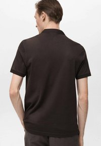 Polo negru cu mânecă scurtă, cu o textură netedă, guler ribitat și o croială lejeră, având un design simplu și curat.