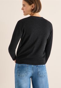 Maglione nero a maglia con maniche lunghe, scollo rotondo e orlo a coste, abbinato a jeans di denim blu chiaro. Texture liscia, design casual.