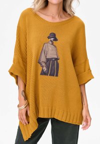 Musztardowożółty, oversize sweter z dzianiny z prążkowaniem na krawędziach, z grafiką modelki w paskowanym stroju na przodzie.