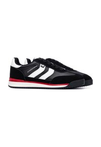 Zapatillas en blanco y negro con una parte superior de ante y cuero, que cuentan con tres rayas blancas, una suela intermedia roja y una suela exterior de goma negra.