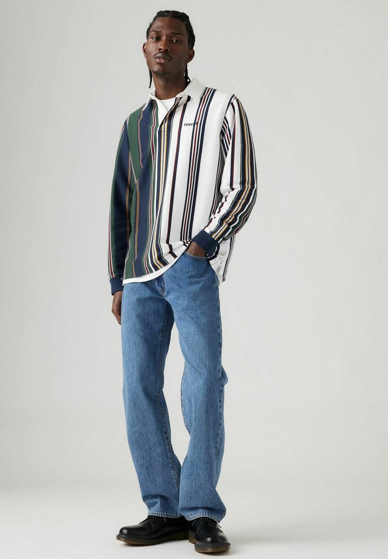 Polo de manga larga a rayas en verde, blanco y azul marino, combinado con jeans azul claro y zapatos negros, con un ajuste relajado y tejido texturizado.