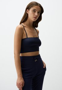 Marineblauwe cropped top met dunne bandjes; glad, rekbaar materiaal; gecombineerd met bijpassende joggingsbroek met elastische tailleband en koord. 