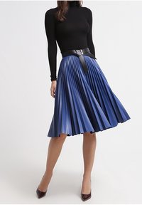 Blå veckad kjol i texturerat material med ett svart bälte i midjan. Bärs med en figurnära svart polo och mörka klackar.