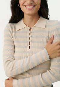 Beež ja heleda halli triibulise kudumi pullover, millel on kraega kaelus ja viis dekoratiivset nööpi esiosal, omab ribakudet ja pikki varrukaid.