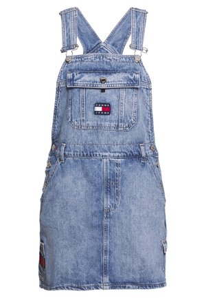 Jasnoniebieska sukienka ogrodniczka z denimu z regulowanymi ramiączkami, przednią kieszenią na klapę z naszywką logo Tommy Jeans oraz guzikami po bokach.