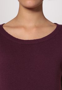 Maglione lavorato a maglia color bordeaux con scollatura rotonda ampia e texture a coste. Tessuto morbido, cuciture sottili e senza decorazioni visibili.
