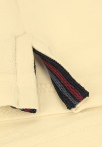 Polohemd aus weichem cremefarbenem Stoff mit gerippten Kragen in Marineblau, Grau und Rot. Verfügt über einen seitlichen Schlitz für zusätzlichen Komfort.