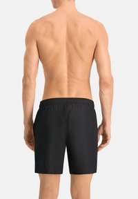 Bañador negro con cinturilla elástica, fabricado con un tejido suave y ligero y un diseño sencillo, cortado hasta la rodilla.