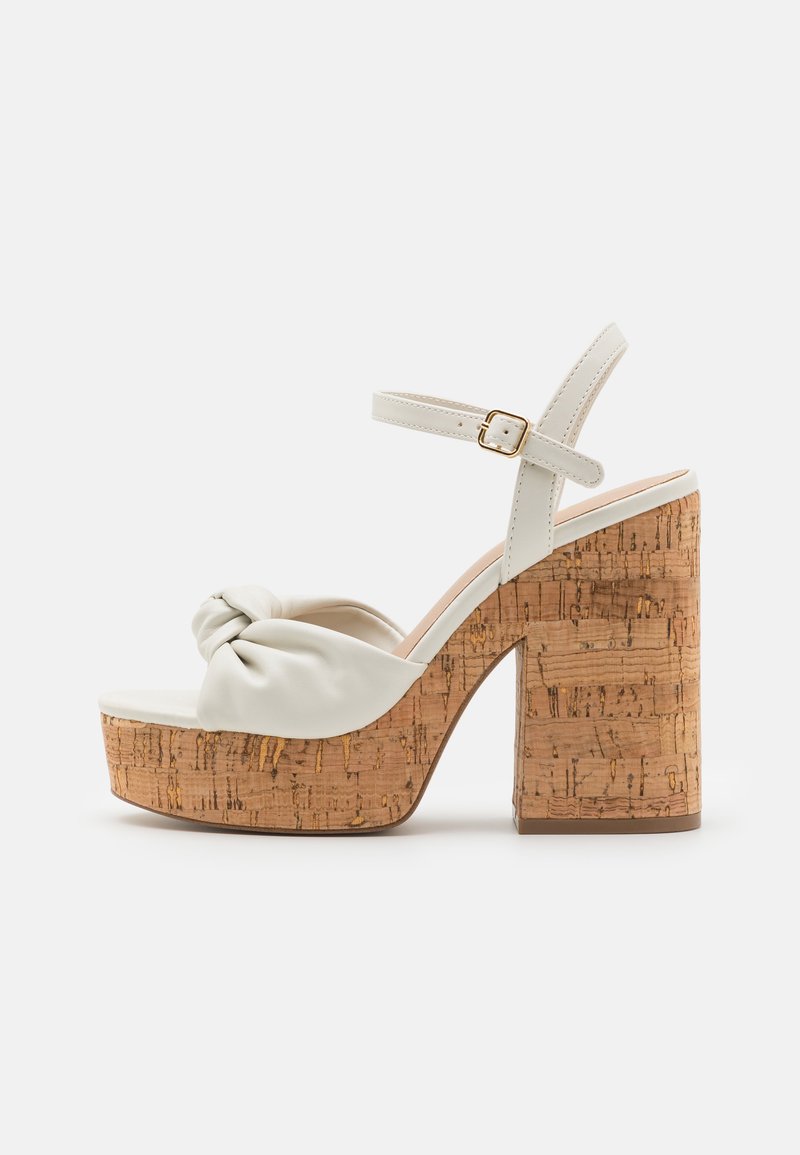 Sandales plates blanches avec un dessus en cuir noué, un talon en liège et une fine bride ajustable à la cheville. Le talon texturé ajoute du détail.