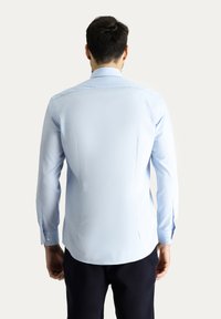Camicia azzurro chiaro a maniche lunghe con colletto classico, design aderente, texture liscia e polsini con bottone. Il retro presenta delle pieghe sottili per dare forma.