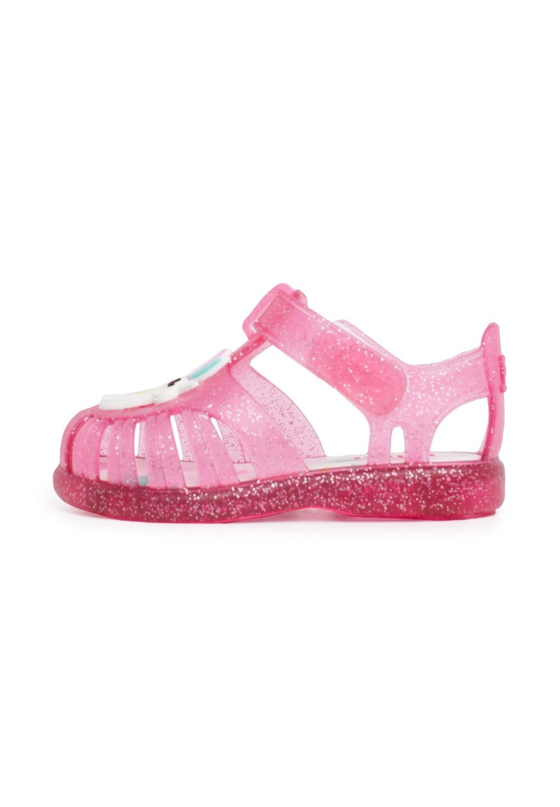 Pink jelly sandal with glitter, open-toe design, adjustable strap, ventilation cutouts, and a decorative front accent. Flat sole.