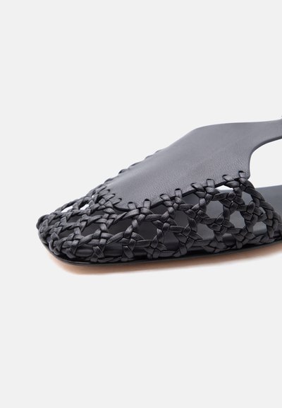Μαύρο δερμάτινο σανδάλι slide με υφαντό σχέδιο στο μπροστινό μέρος και συμπαγές πάνω τμήμα, παρουσιάζεται σε απλό ανοιχτό φόντο.