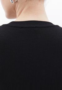 Top nero a coste con scollatura rotonda. Il tessuto presenta una texture a righe verticali, mostrando la parte posteriore del collo e le spalle.