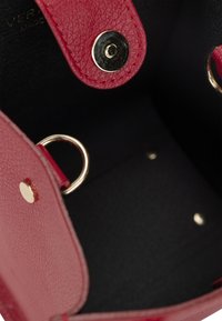 Innenansicht einer roten, strukturierten Lederhandtasche mit goldenen Hardware-Akzenten, einschließlich Druckknöpfen und Metallringen, auf einem schwarzen Innenfutter.