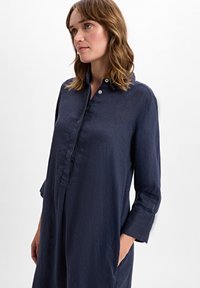 Navy-blaues Leinenkleid mit umlegbarem Kragen, langen Ärmeln und seitlichen Taschen. Hat eine lockere Passform und eine dezente Textur.