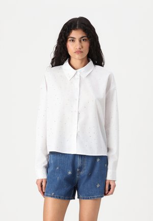 White button-up shirt with subtle metallic dot pattern, long sleeves, and a rounded collar, paired with denim shorts featuring embroidery.
