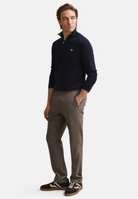 Marinblå sweater med kvartszip, grå texturerade byxor och mörka sneakers med vita accenter. Modellen står med händerna i fickorna mot en vit bakgrund.