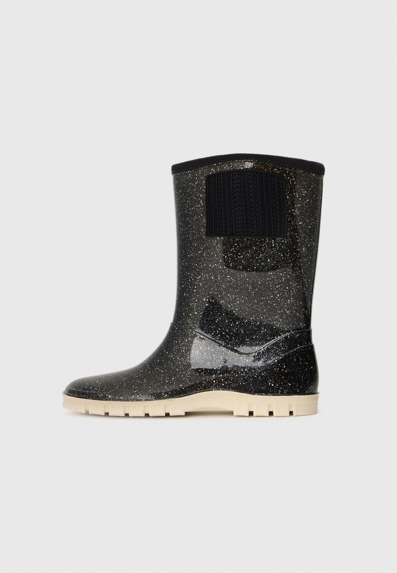 Botte en caoutchouc noire mouchetée mi-mollet avec semelle beige à relief et tirant noir texturé sur surface lisse et imperméable.