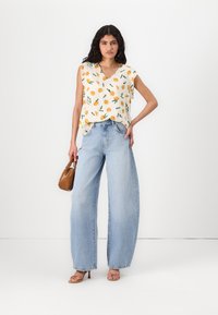 Blommönstrad, ärmlös krämfärgad topp med orange och gröna accenter; ljusblå vida jeans; brun handväska; remsandaler.