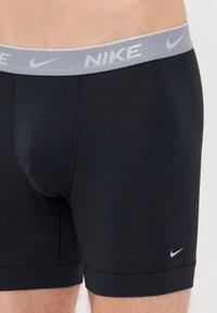 Črne atletske bokserice z gumo sive barve, na kateri je napis "NIKE", ter majhnim logotipom Nike swoosh na spodnji levi strani.