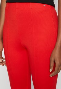 Leggings rossi realizzati in tessuto testurizzato, con una vestibilità aderente e cuciture verticali. Un piccolo dettaglio con il logo vicino alla vita.