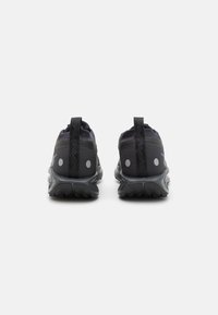 Chaussures de sport noires avec un dessus texturé, des accents réfléchissants et une semelle extérieure robuste avec des rainures de traction. Onglet à l'arrière pour un enfilage facile.