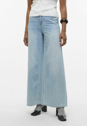 Lichtblauwe wijde spijkerbroek van denim, met een hoge taille en schone naden. Gecombineerd met zwarte hakken en grijze sokken.