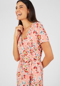 Vestido de wrap floral en suave tela rosa con flores rojas, azules y amarillas. Las mangas cortas y un detalle de cinta en la cintura completan el diseño.