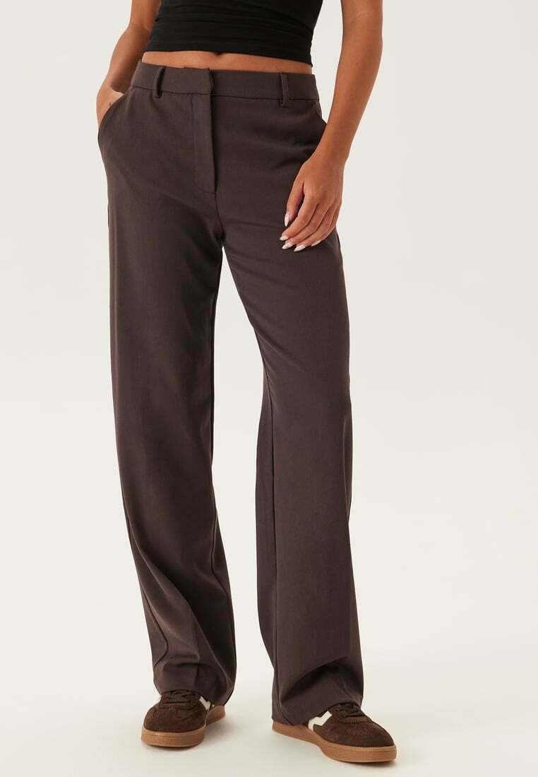 Vidbenade byxor i mörkbrunt tyg, med en slät yta och framfickor, kombinerat med bruna mockaskor.