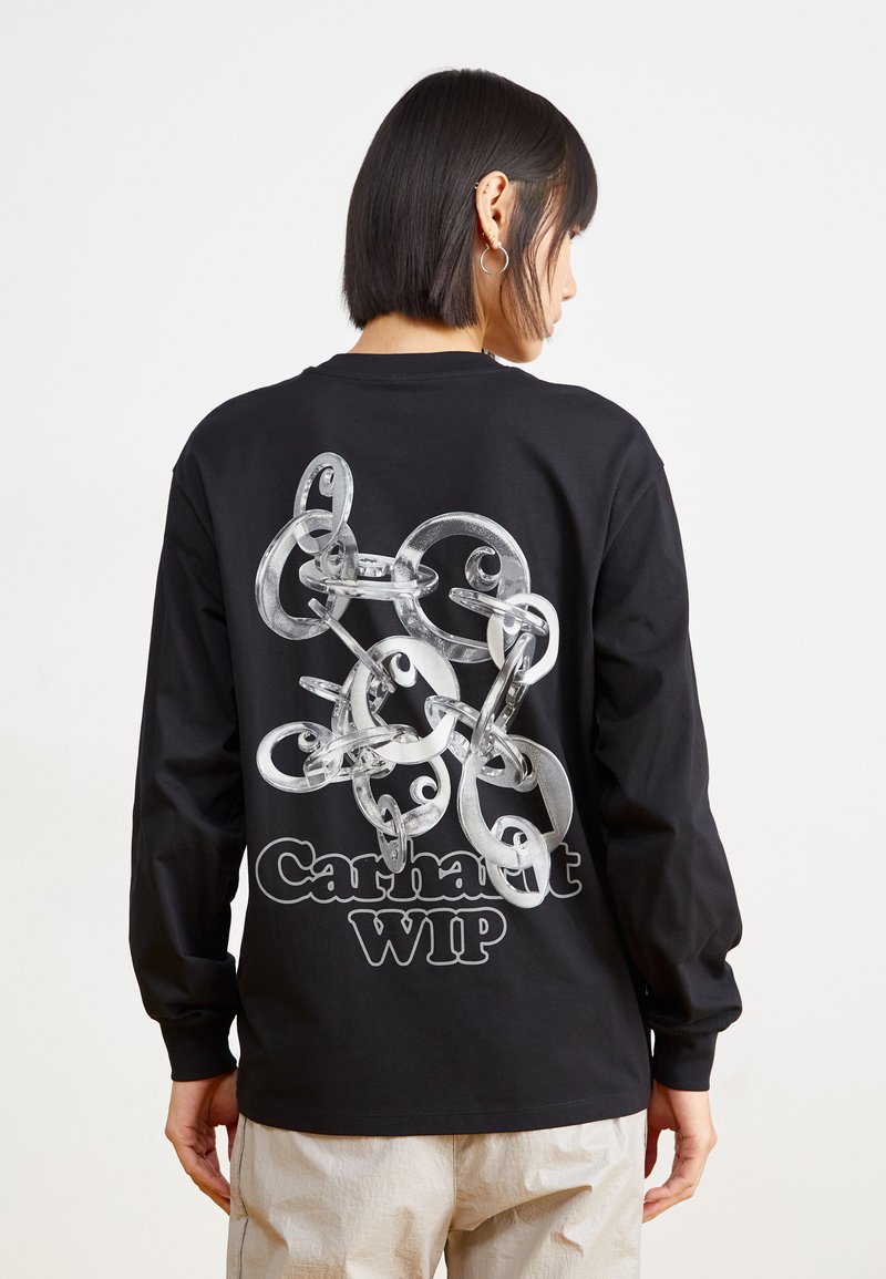 Melns garām piedurknēm krekls ar grafisko dizainu, kurā redzami savienoti caurspīdīgi gredzeni uz aizmugures, ar tekstu "Carhartt WIP" zemāk.